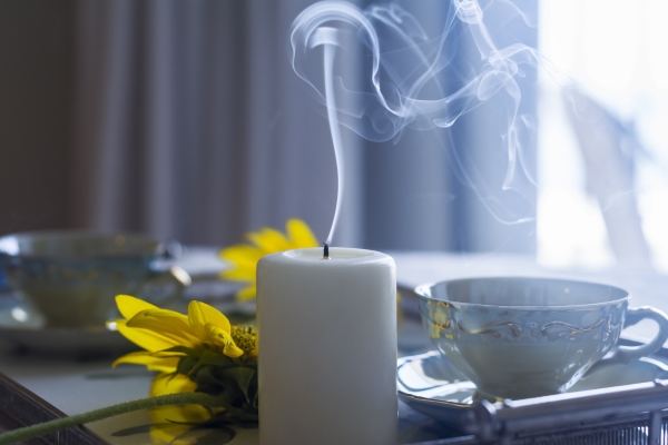 White candle with smoke coming from top sitting next to a tea cup and yellow flowers