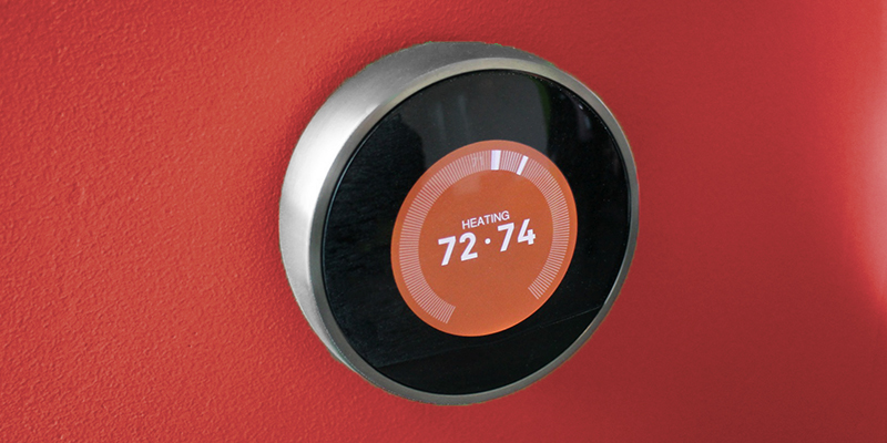 Smart thermostat on dark orange wall reading 72-74