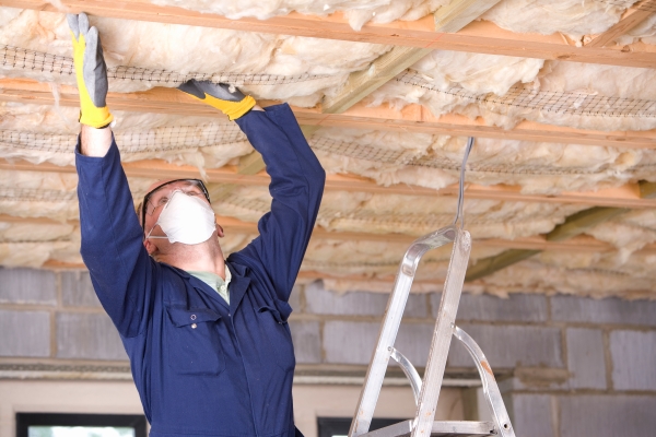 Man wearing a mask putting insulation in a ceiling
